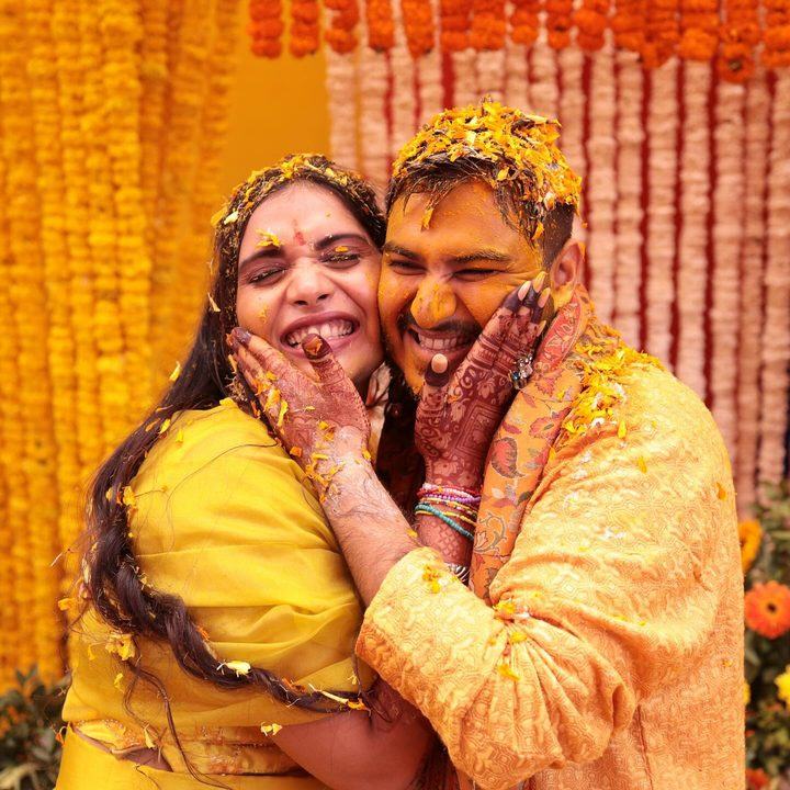Bride and groom laughing together covered in Haldi petals