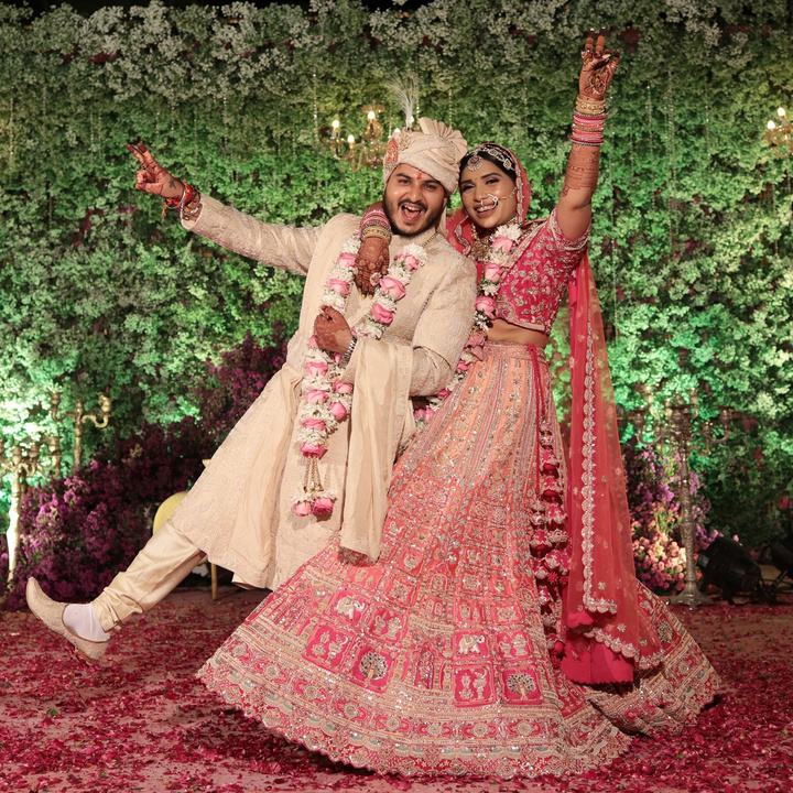 Bride and groom celebrating with raised hands under a floral wall